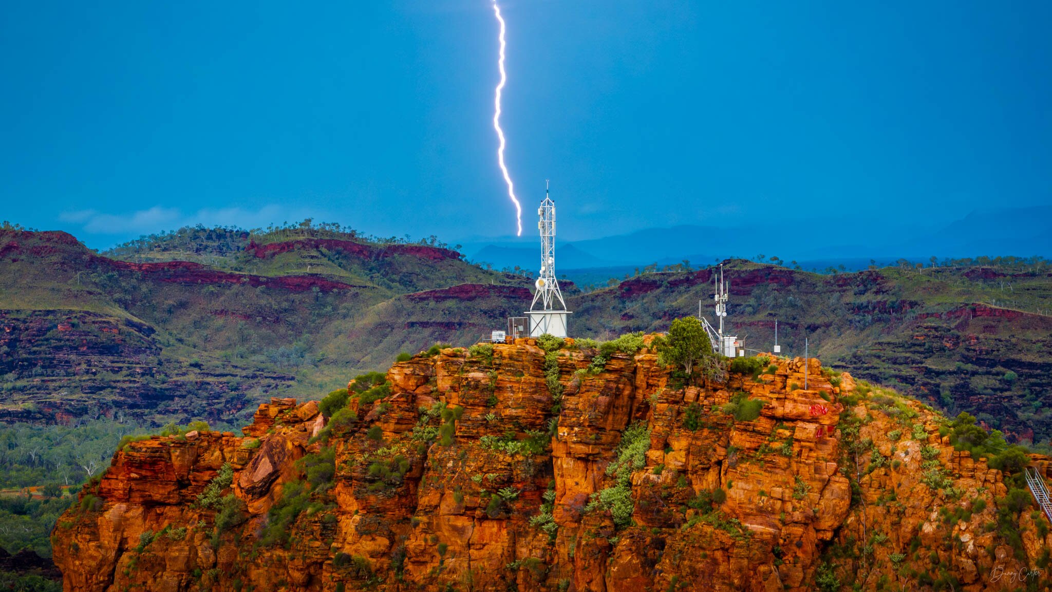 Lightning strikes hills behind a red rocky outcrop during a Kimberley storm