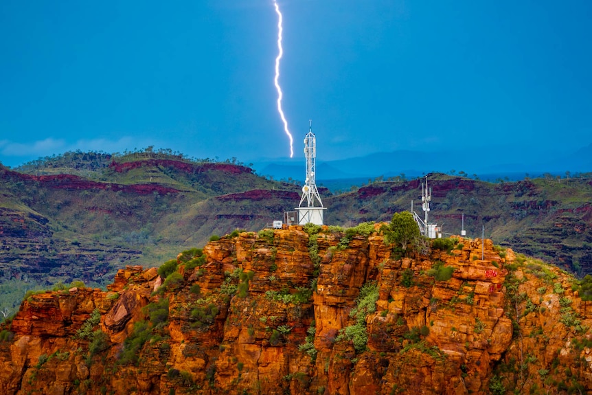 Lightning strikes hills behind a red rocky outcrop during a Kimberley storm