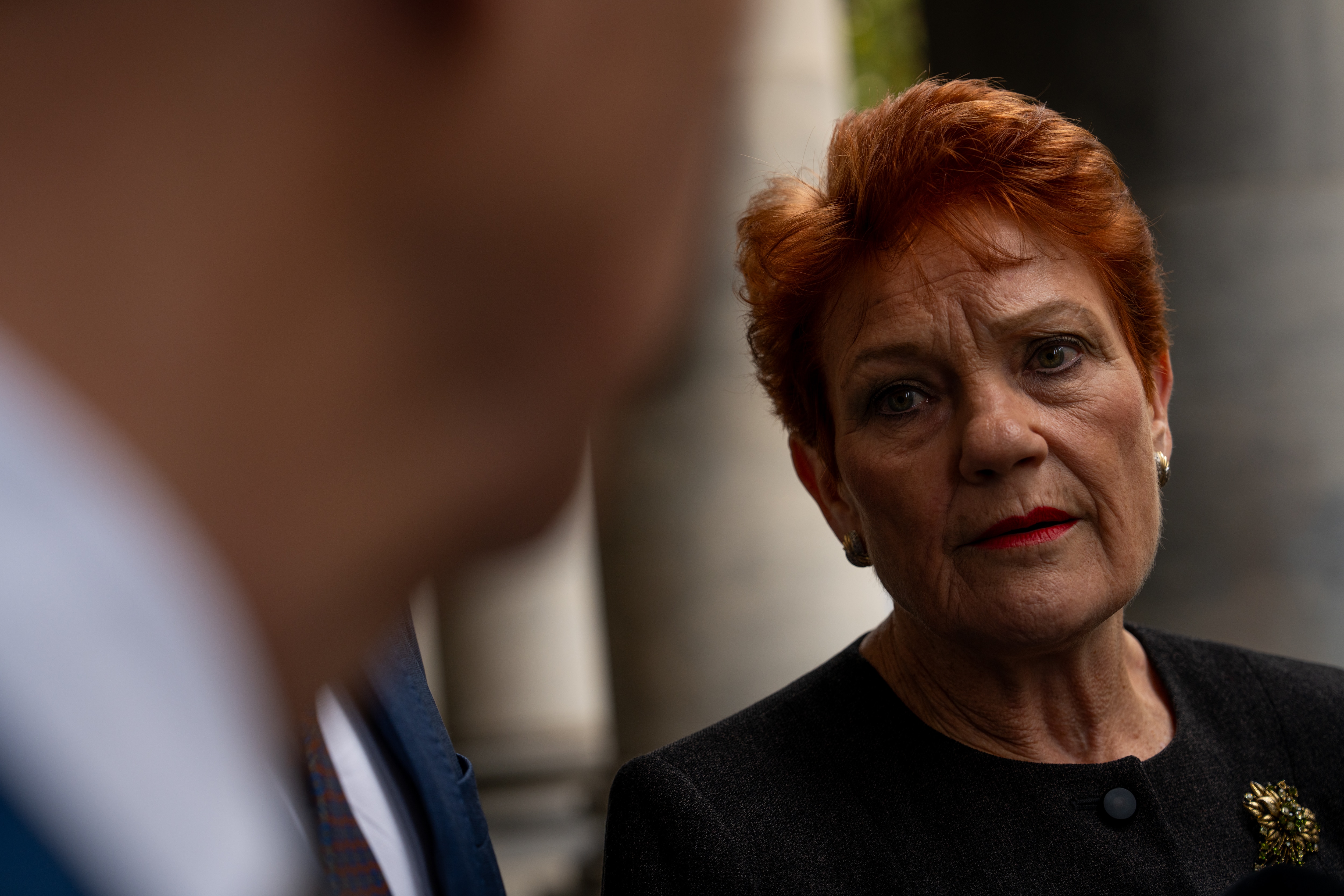 A woman with short, red hair, wearing a black jacket, looking at a man who is out of focus.