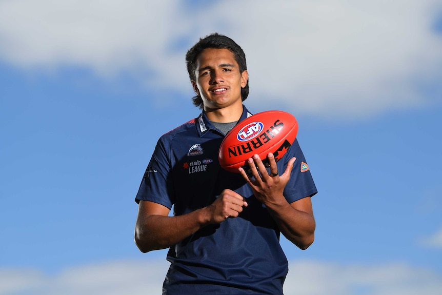 A young AFL prospect handballs the ball to himself as he stares at the camera.