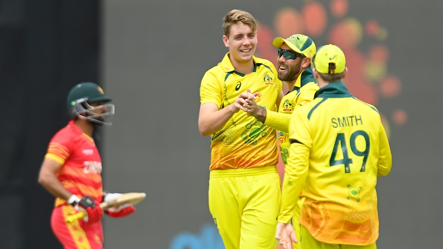 An Australian bowler smiles as he receives congratulations from teammates while a dismissed Zimbabwe batsman walks off.
