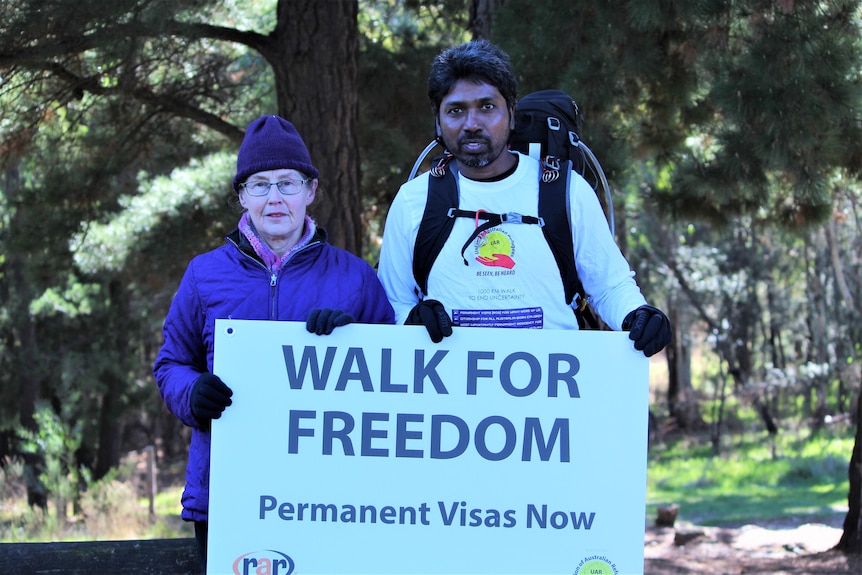 A woman and man hold a sign that reads, "Walk for freedom", standing on a hiking trail.