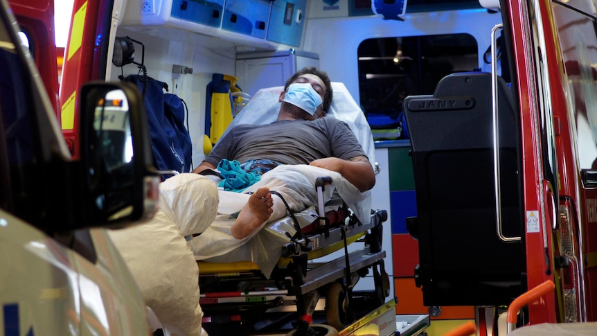 A man wearing a face mask lies in an ambulance