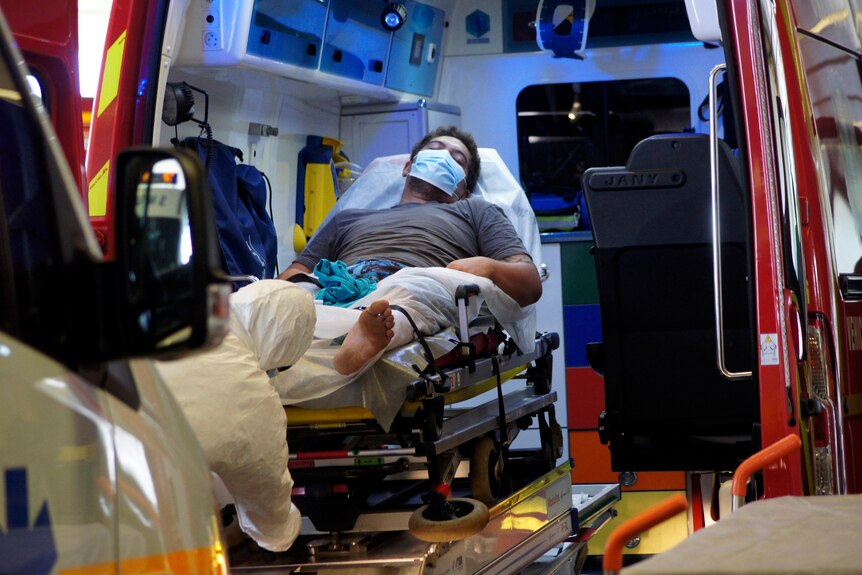 A man wearing a face mask lies in an ambulance