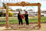 Two women standing in a frame with gardens of flowers and ferris wheel behind them