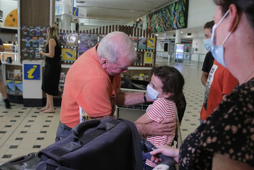 An old man hugs a little girl in an airport.