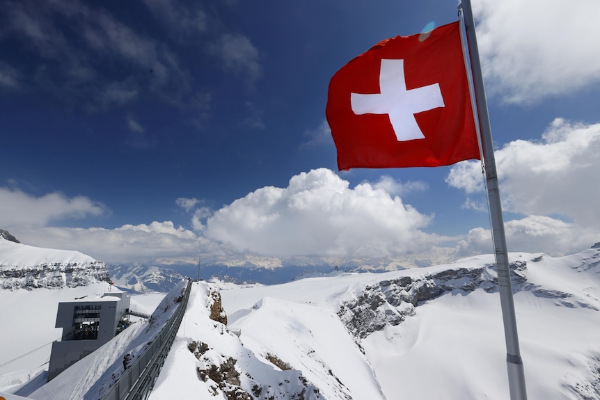A Swiss flag flies amid snowy mountains. 