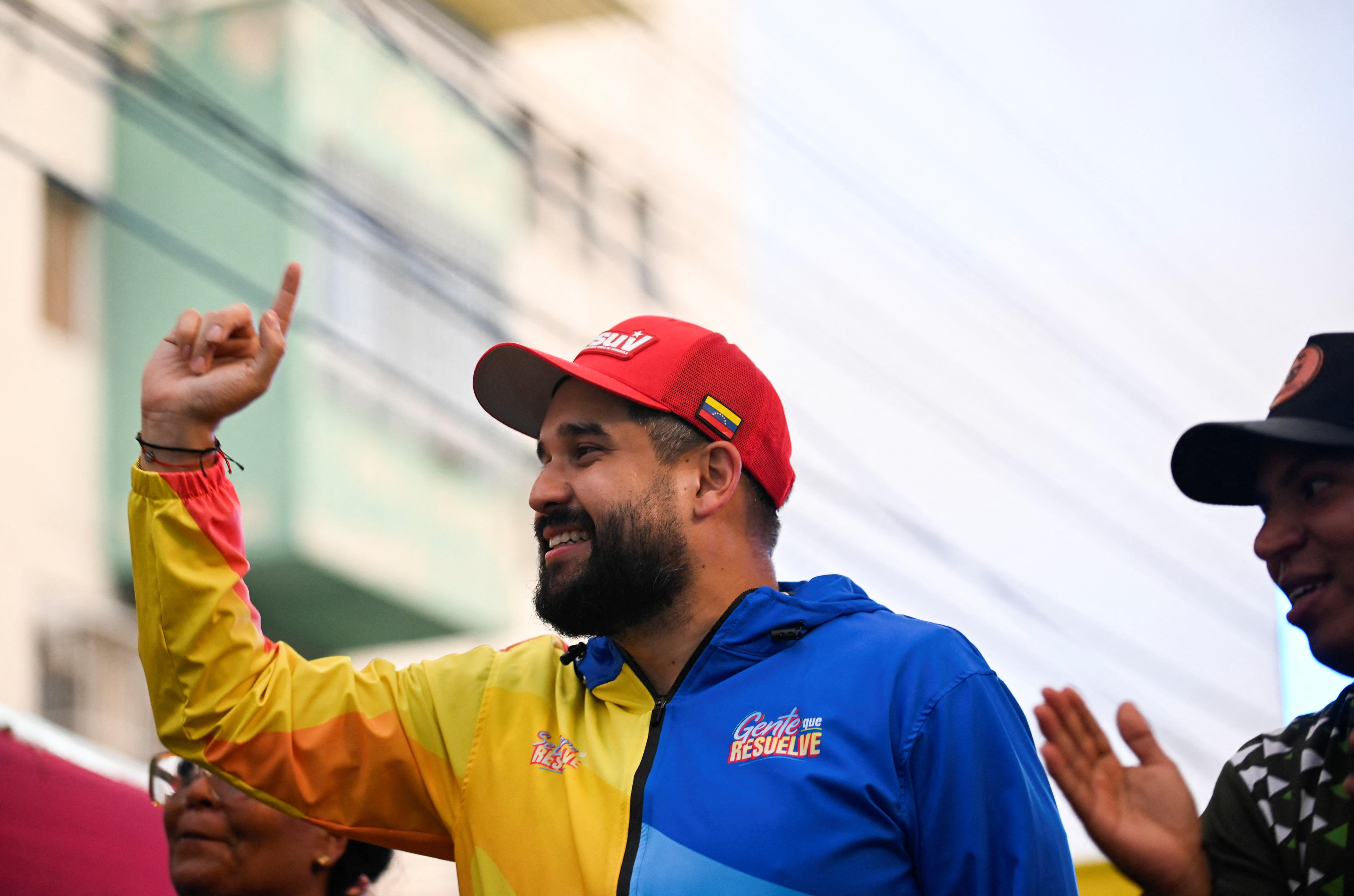 Un hombre con una chaqueta y un sombrero coloridos levanta un dedo.