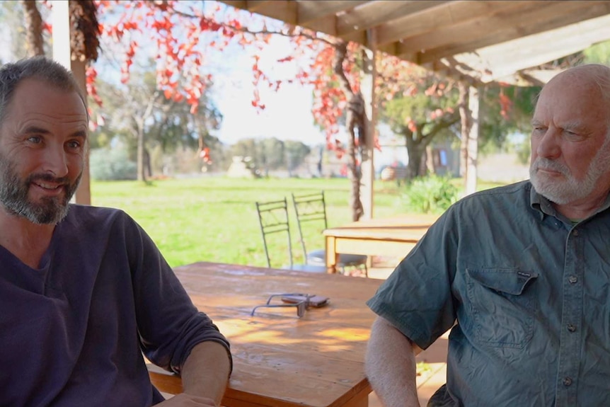 Two men sitting at the corner of a table on a patio