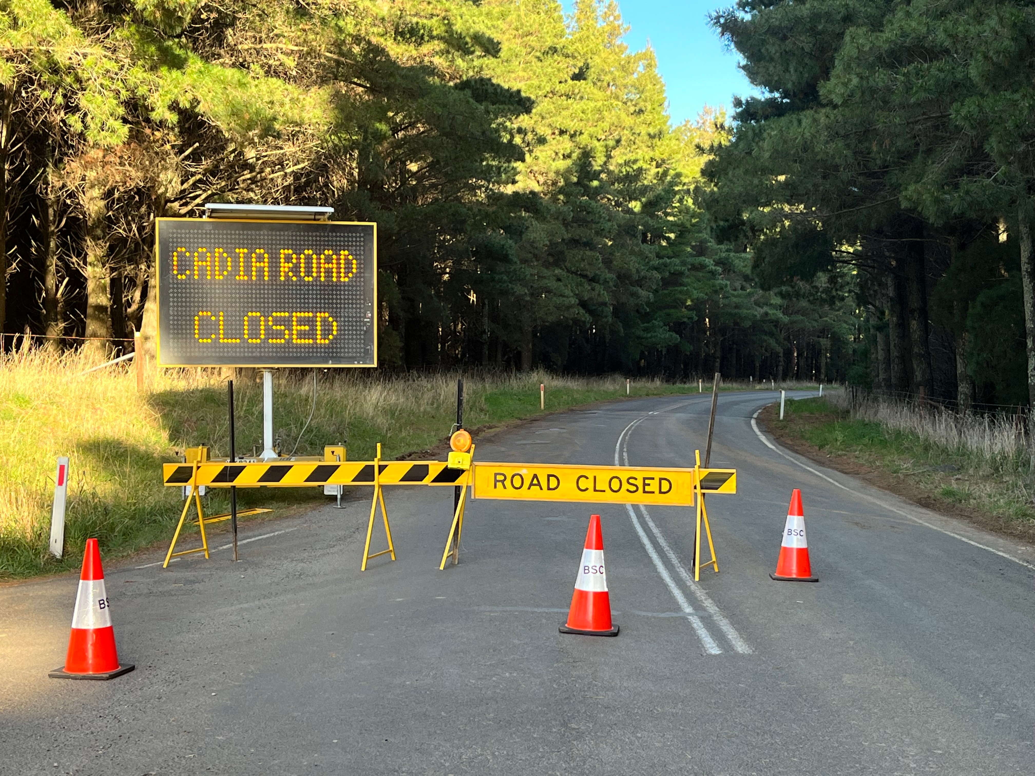 Road closed sign and road closed barriers across bitumen road 