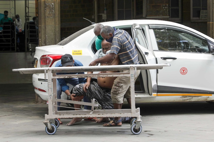 Three men help a semi-conscious men out of a taxi onto a nearby hospital stretcher