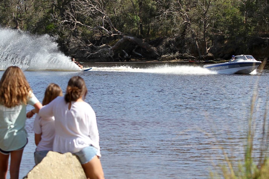 Photo from behind of children standing on the shore watching a water-skier behind a boat on the Kalgan River.