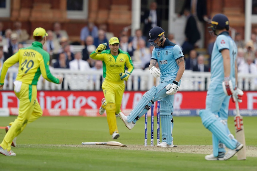 Ben Stokes kicks at his cricket bat, which lies flat on the ground. Around him, Australian players have begun celebrating.