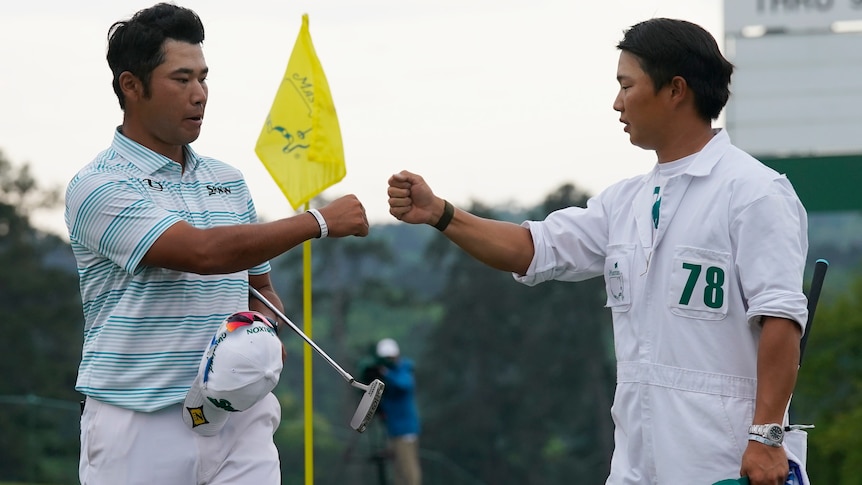 Hideki Matsuyama fist bumps with his caddy with the flag stick in the background