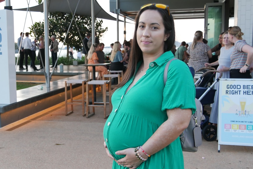 A pregnant woman in a green dress holding her belly in front of a small crowd