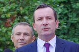 A mid-shot of Mark McGowan talking into microphones at a media conference outdoors.