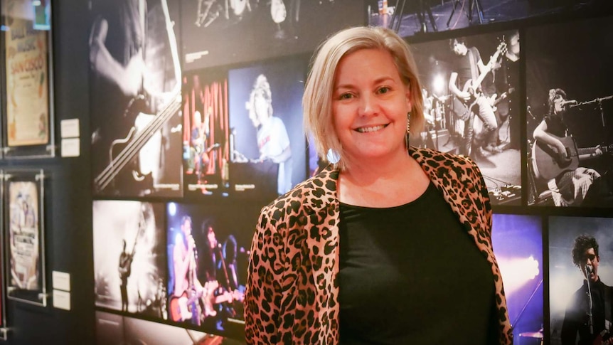 Lady standing in front of a wall of music photographs.