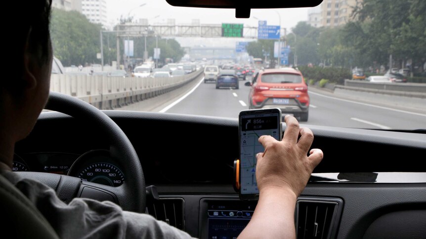 A driver looks at his Didi rideshare app while driving down a road in Beijing