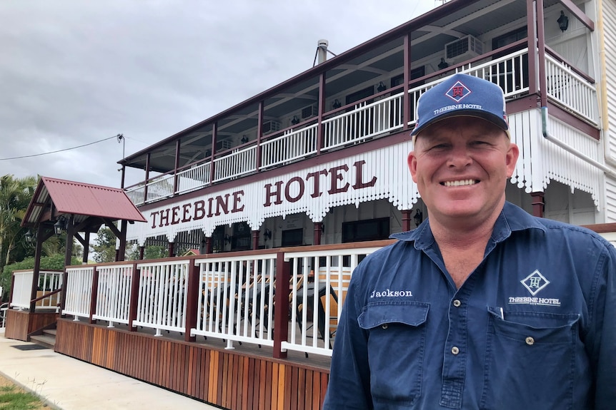 A man in a cap smiles at the camera with the Theebine hotel and new front deck behind him.