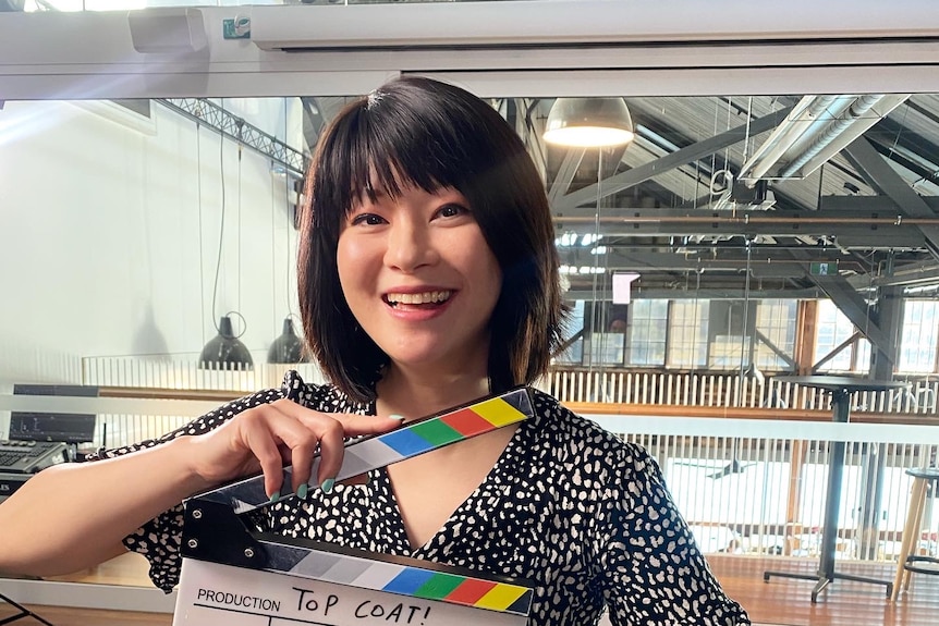 Michelle Law sitting on a chair with a director's production clapping board 