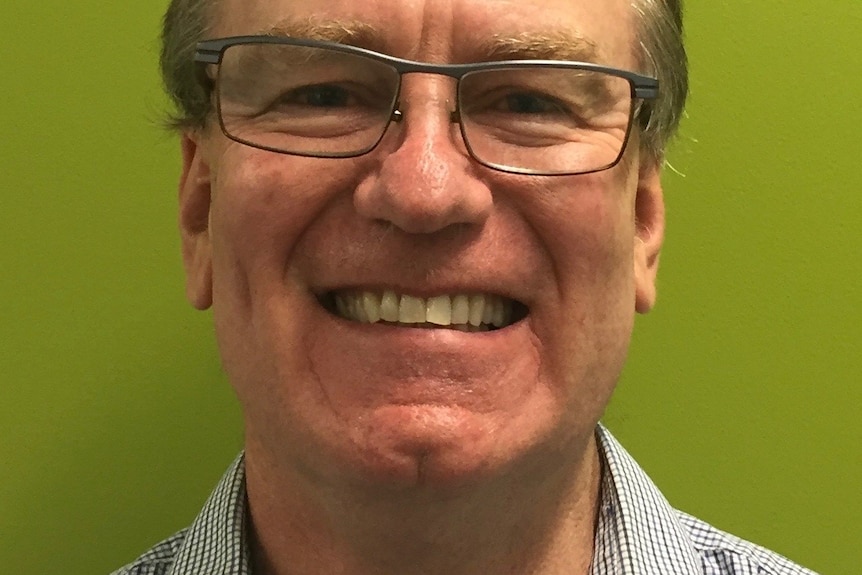 A headshot of a middle-aged man wearing glasses smiling at the camera.