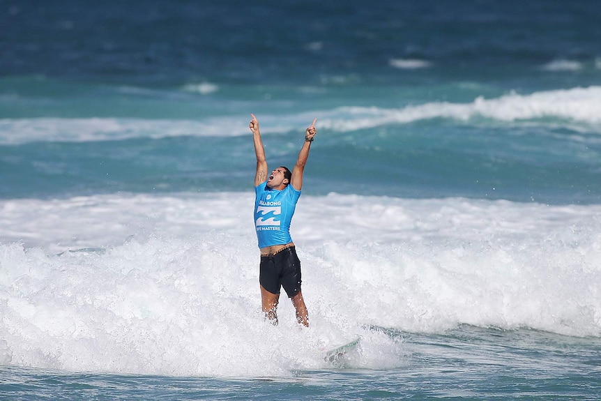 Adriano De Souza stands upright on his board and points skywards with both arms raised after winning the world surfing title.