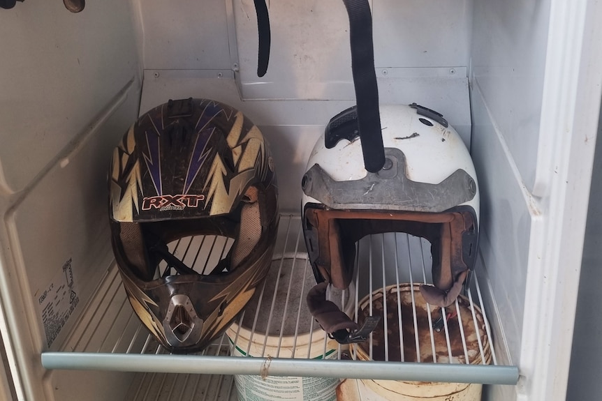 Four motorbike helmets are stored in an old fridge. They're dirty and look well used. 