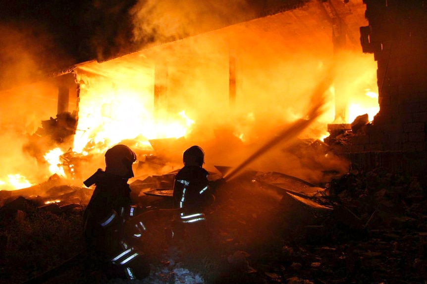 Two firefighters silhouetted against flames that have engulfed a building
