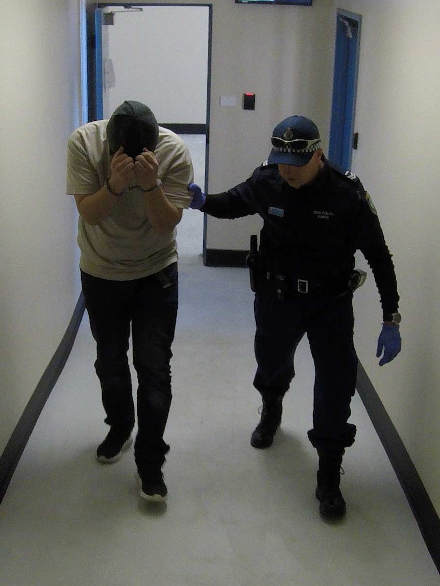 A law enforcement officer leads a handcuffed suspect of illegal narcotic activities.