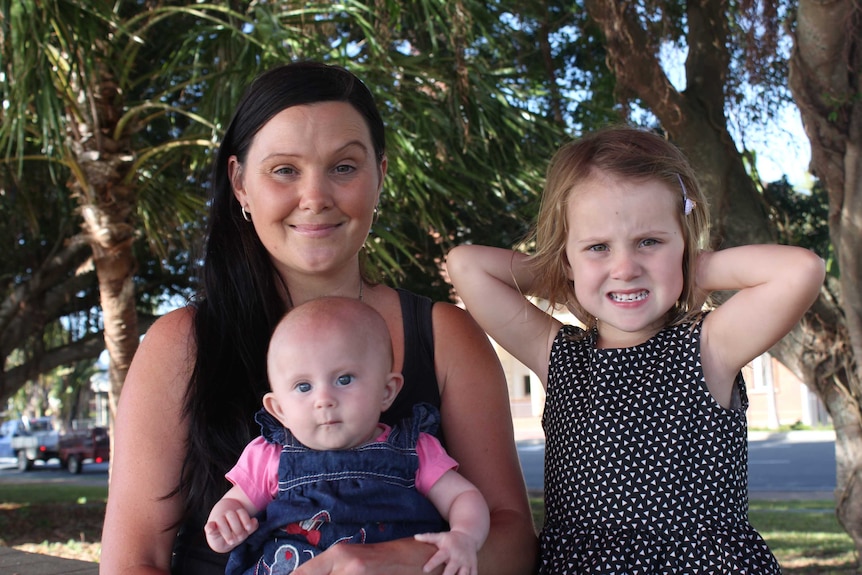 A woman holds a baby and sits next to a young girl