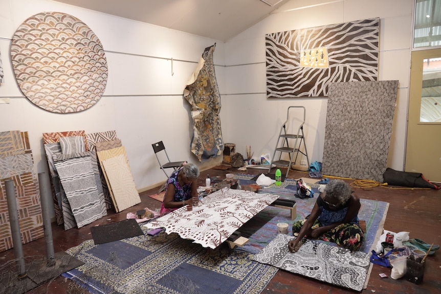 Yolŋu artist Naminapu Maymuru-White sits down painting in a room with another artist.