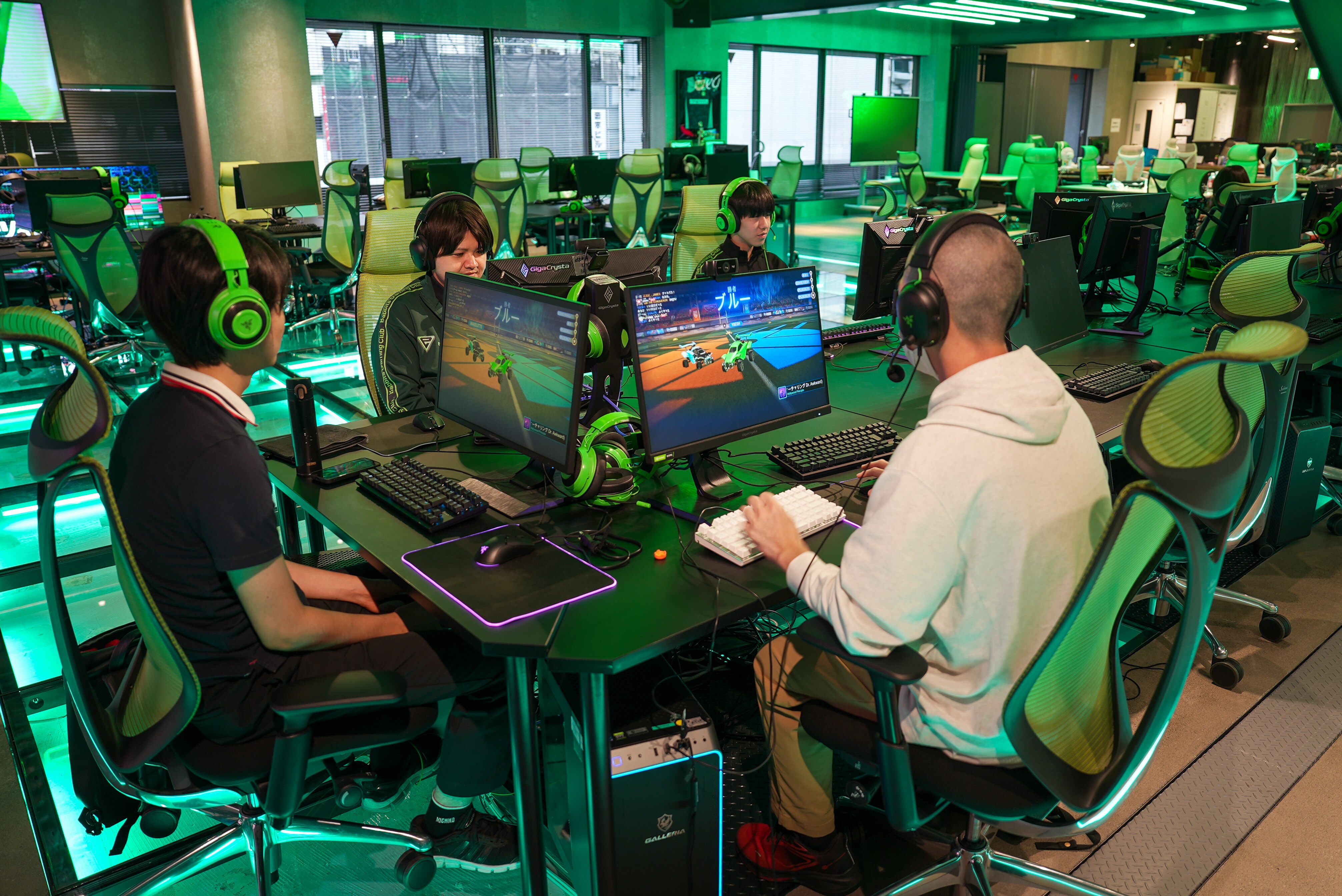 Três homens com fones de ouvido estão sentados em uma sala cheia de mesas e computadores.