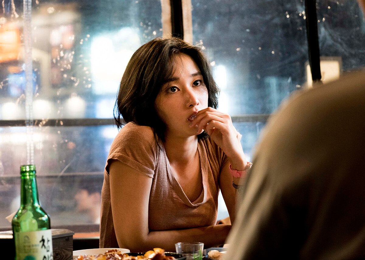 Colour still of Jun Jong-seo sitting at table in restaurant at night time in 2018 film Burning.