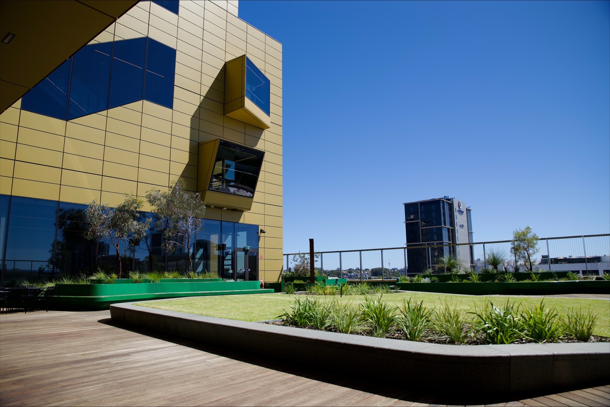 Um edifício de vários andares cor de mostarda com terraços e gramados ao redor. 