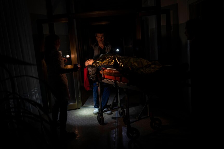 A man pushes an injured boy on a stretcher in the dark. 