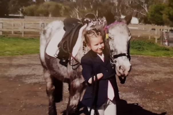 A young blonde child with no forearms in an old photo of her with a horse.