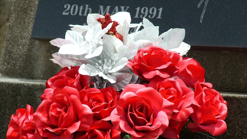 Fake red and white flowers in front of a gravestone.