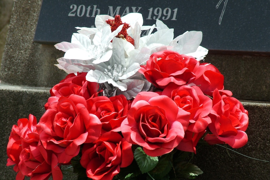 Fake red and white flowers in front of a gravestone.