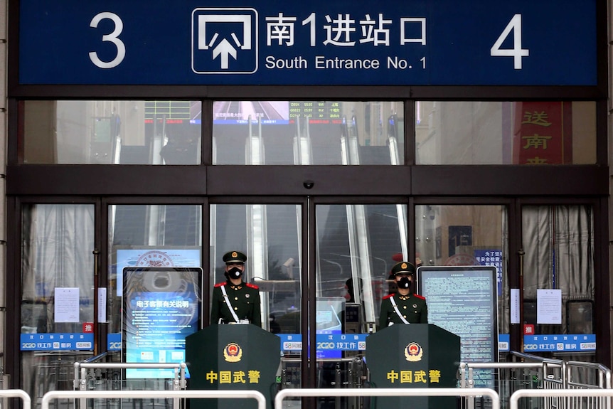 Two guards in masks stand at attention outside a Wuhan station