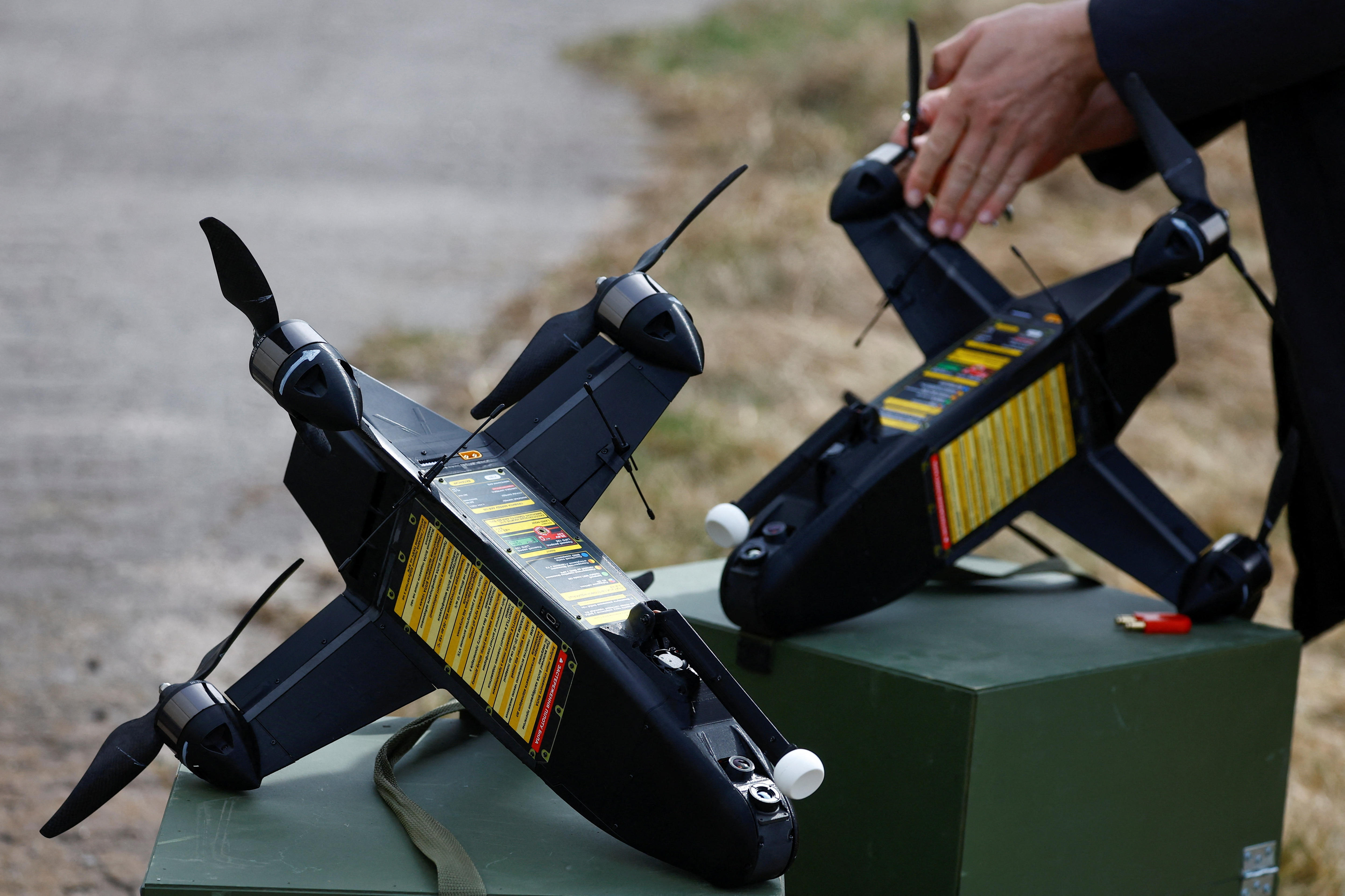 Two small drones on the ground, with a person's hand attaching a rotor blade to one of them.