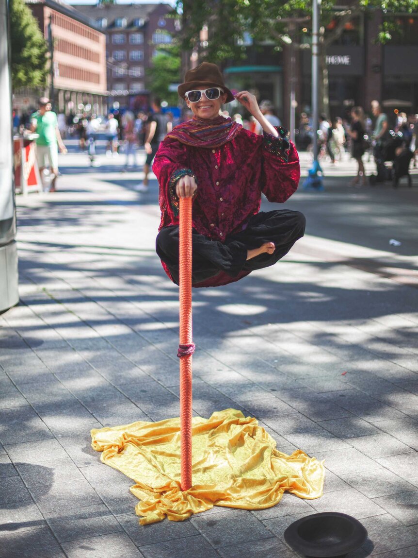 Cross-legged person appearing to float in mid-air while holding onto an orange pole.