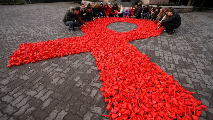 People gather around a massive HIV red ribbon tribute laid out on the ground.