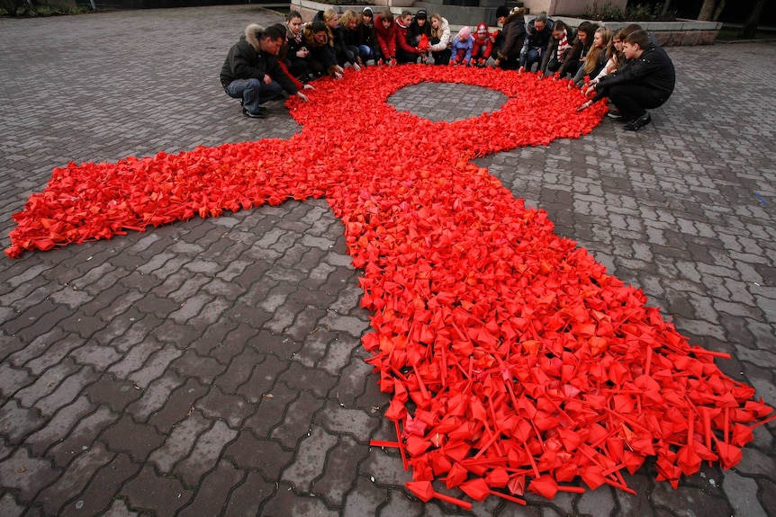 People gather around a massive HIV red ribbon tribute laid out on the ground.