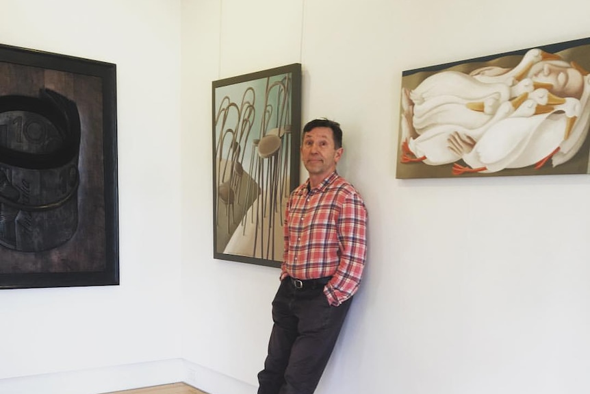 A man leans against a wall between two paintings