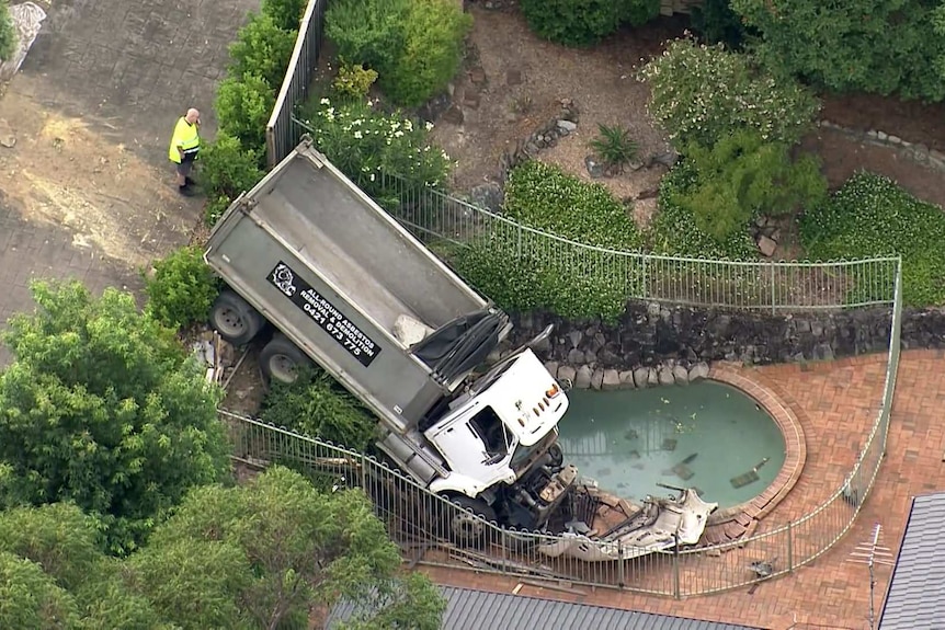 A truck with an empty tray with the front of it landing just right of a gated pool