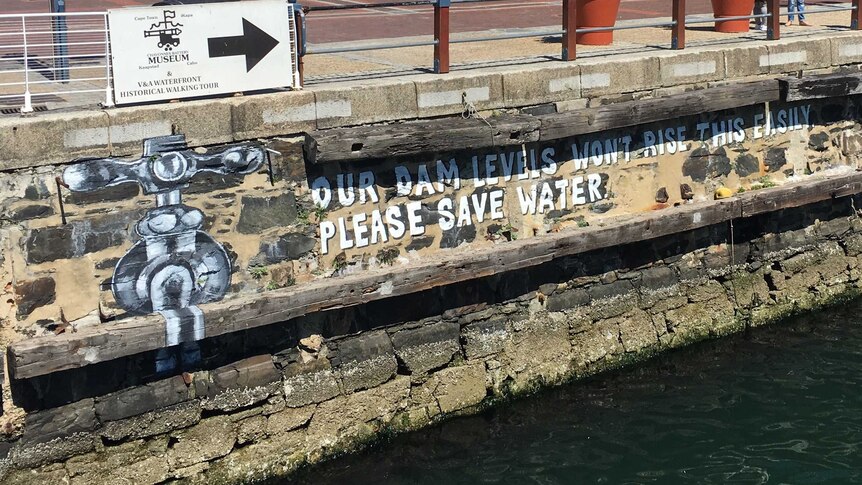 A mural above the harbour that says "our dam levels won't rise this easily, please save water"