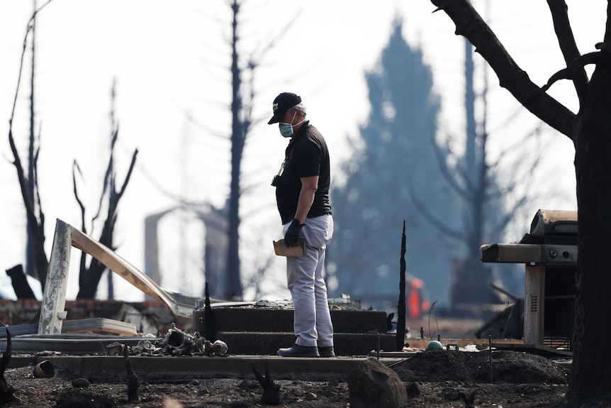 Retiree Kaan Chin stands on the rubble of his home wearing a protective mask and gloves