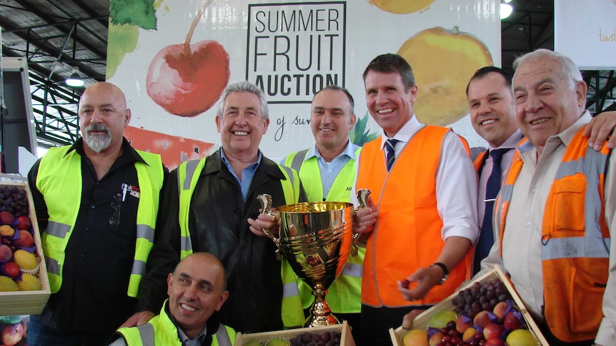 The NSW Premier Mike Baird and men from the Sydney Markets hold a gold trophy and boxes of summer fruit.