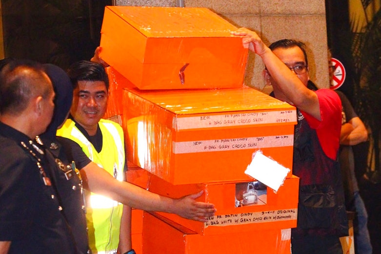 Malaysian police with a trolley full of orange boxes of confiscated items