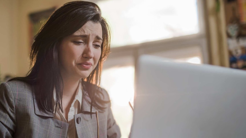 A young woman in business attire looks upset while staring at a laptop.